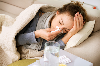 woman sick with the flu lying on couch with blanket and tissues