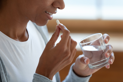 close up of woman taking a supplement with a glass of water