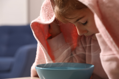 little girl breathing in steam from bowl with towel over her head
