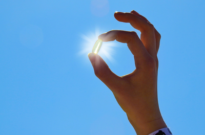 vitamin D supplement held up against the sun in blue sky