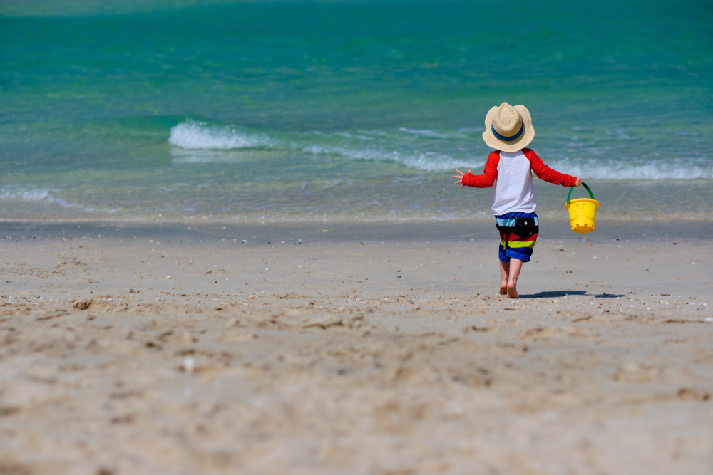 little boy wearing long sleeves  and hat on beach