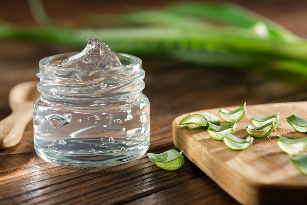 clear jar of aloe vera gel next to slices of aloe vera plant