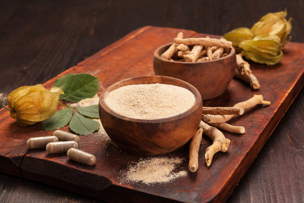 ashwagandha roots, powder, and capsules on a wooden tray