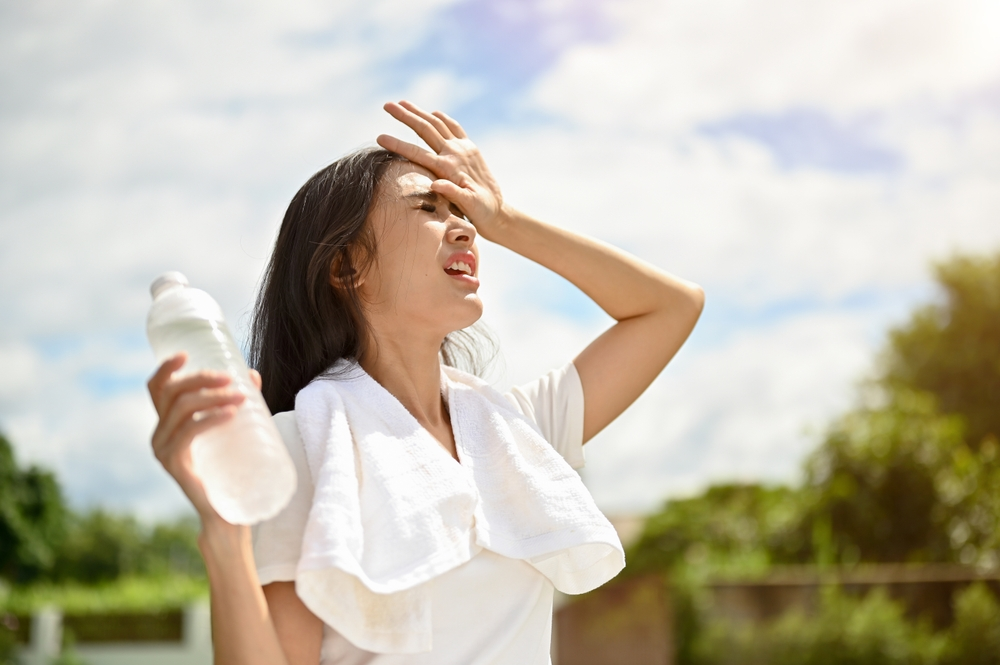 young woman sweating outside with towel around shoulders and cold water bottle in hand